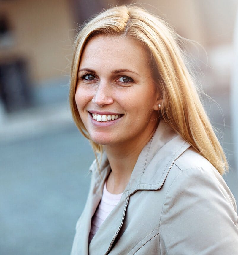 blond woman with long hair smiling in front of a building