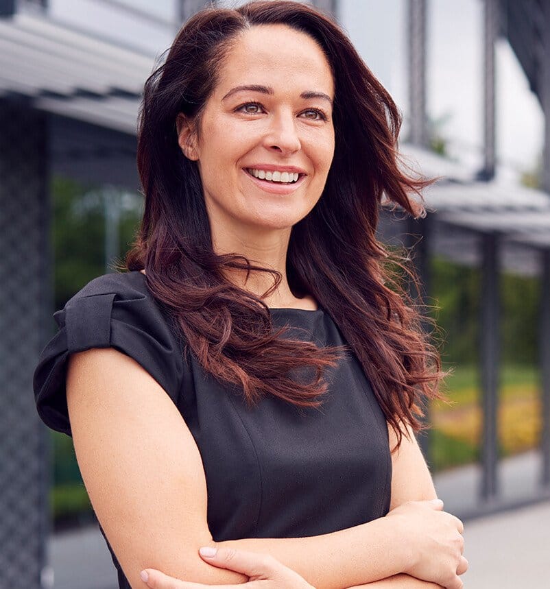 smiling woman in black dress standing outside of a building with her arms crossed