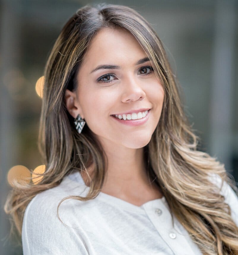 smiling woman with long hair and earrings standing in front of a building