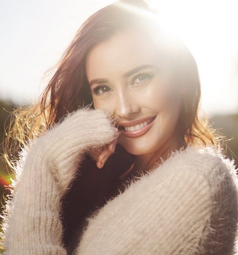 Woman with red hair smiling outside with the sun shining behind her