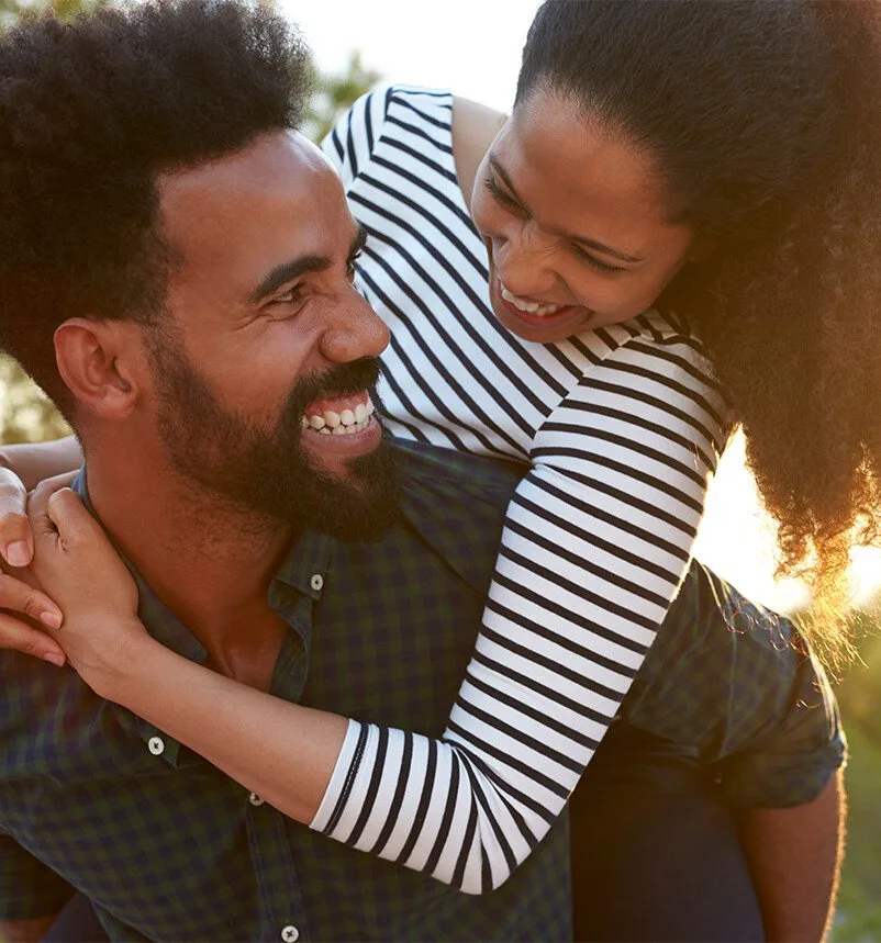 smiling man carrying a woman on his back in a park