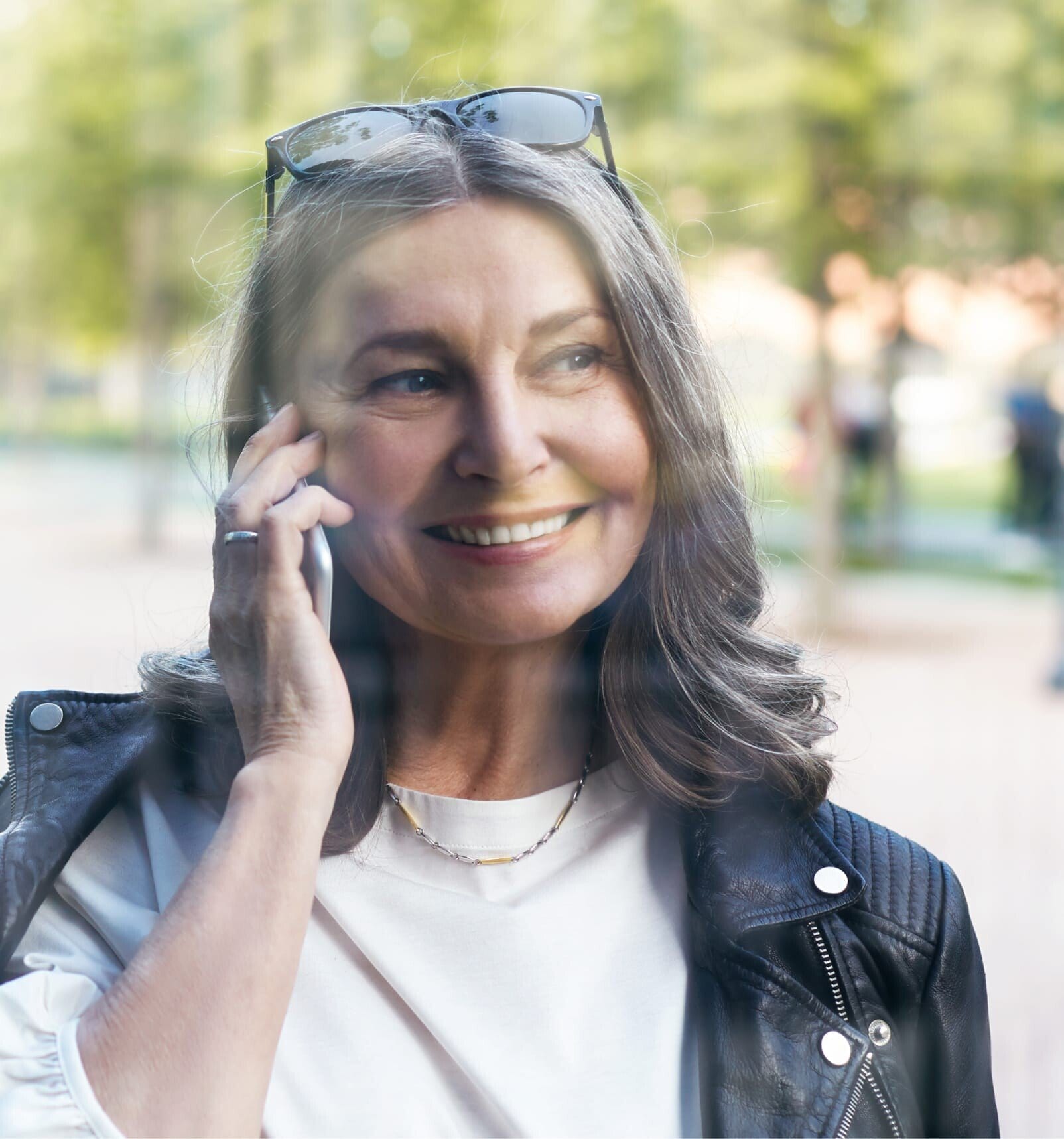 smiling woman in leather jacket talking on cell phone in park