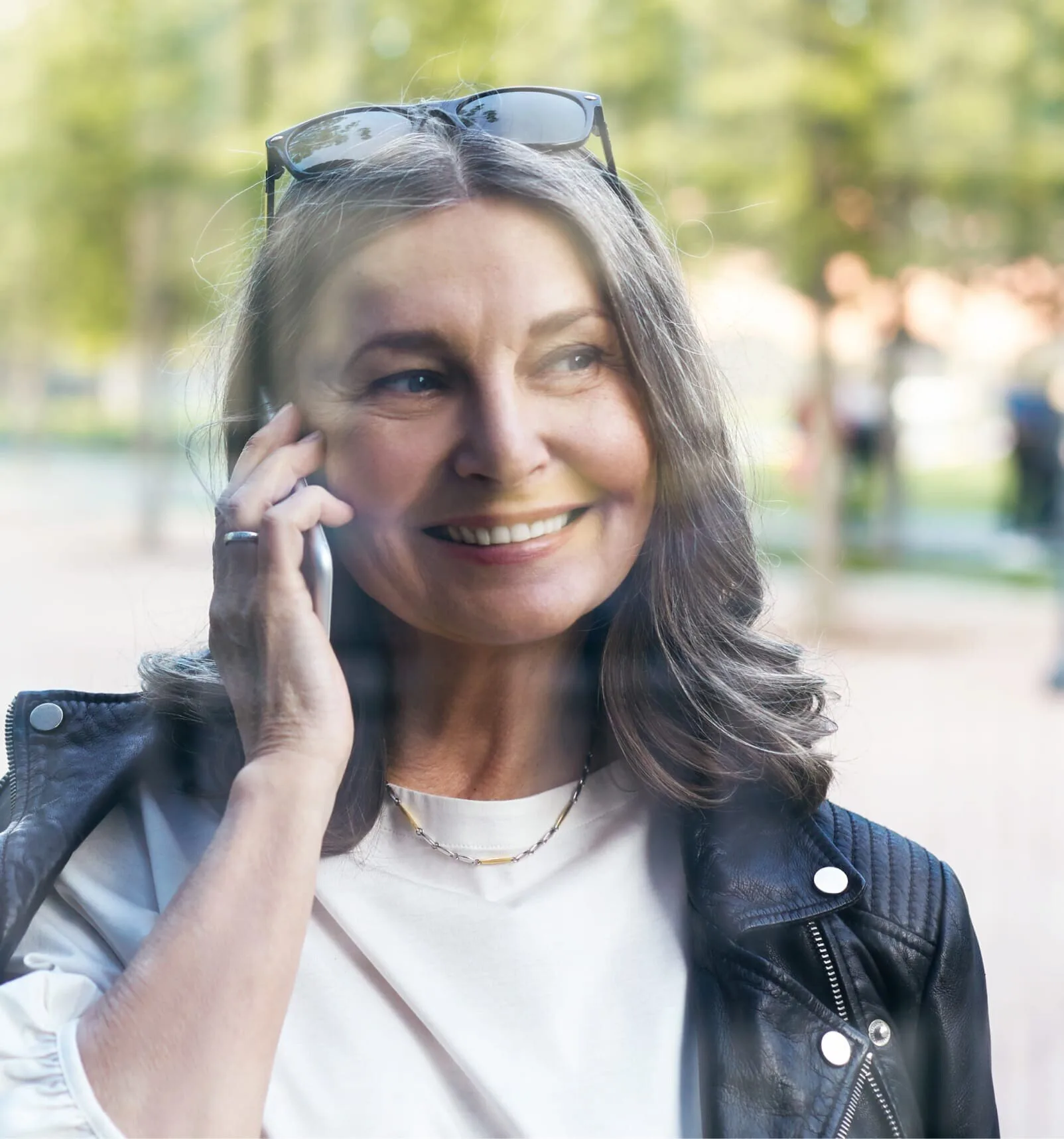 smiling woman in leather jacket talking on cell phone in park
