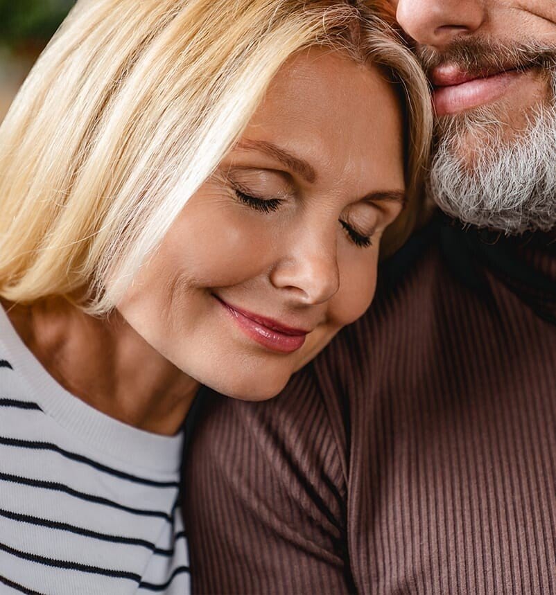 blond woman with eyes closed and man with beard looking at her