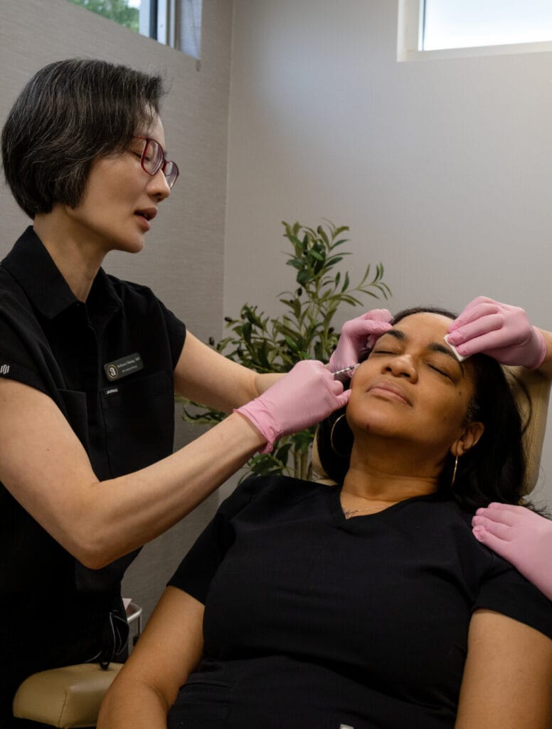 Dr. Chiang performing a neurotoxin treatment on a patient in a modern, clinical setting. The doctor is focused, holding a syringe with precision, while the patient appears relaxed. The bright, clean aesthetic of the room emphasizes a professional and calm medical environment.